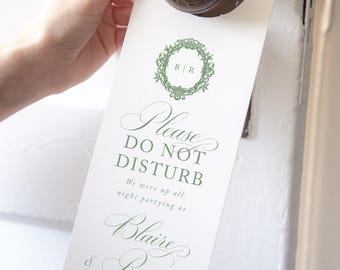 May include: A white rectangular door hanger with green text and a circular wreath graphic. The text reads: Please DO NOT DISTURB We were up all night partying at Blaire & Roger's wedding 05.15.2021. The hanger features a circular cutout at the top.