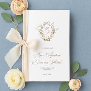 May include: A wedding invitation with a floral wreath and ribbon. The invitation reads "The Wedding Of Reese Marlowe & Dawson Whitaker" with the date 06.10.2023. The invitation is decorated with flowers and greenery on a blue background.