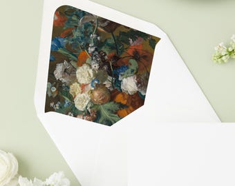 May include: White envelope with a floral design on the inside. The floral design features a variety of flowers in shades of white, orange, blue, and brown. A white card is next to the envelope. A green plate is in the background.