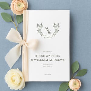 May include: A wedding invitation with the names Reese Walters and William Andrews, adorned with a cream-colored ribbon and floral accents. The invitation includes the wedding date and location, Myrtle Beach, SC.