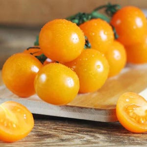 May include: A cluster of small, bright orange tomatoes on a wooden cutting board. The tomatoes are arranged in a pyramid shape, with the largest tomato at the top and the smallest tomatoes at the bottom.