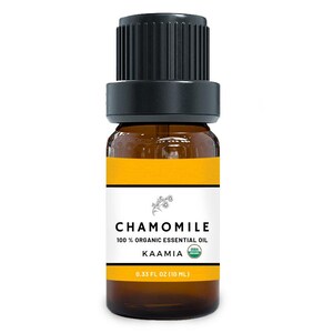 May include: A small amber glass bottle of essential oil with a black ribbed cap. The white label features the text CHAMOMILE, 100% ORGANIC ESSENTIAL OIL, KAAMIA, and 0.33 FL OZ (10 ML) with a small USDA Organic seal and a floral illustration.