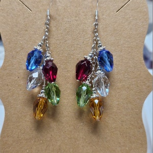 May include: A pair of dangle earrings with a silver chain and multi-colored crystal beads. The beads are in shades of blue, red, green, and amber.