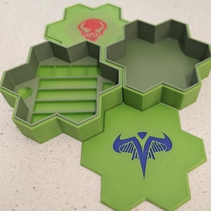 May include: Hexagonal green storage containers with gray trim. One container is open, revealing interior compartments. Two lids feature red and blue graphic designs. The containers are designed to interlock.