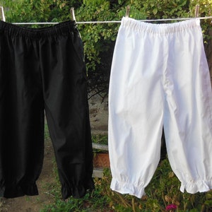 May include: Two pairs of white and black cotton bloomers hanging on a clothesline. The bloomers have a gathered elastic waistband and ruffles at the bottom.