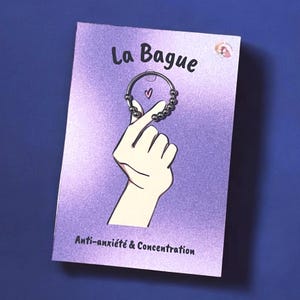 Puede incluir: Una tarjeta morada con el texto "La Bague" y "Anti-anxiété & Concentration" en negro. Una mano de dibujos animados sostiene un anillo plateado con pequeñas cuentas.