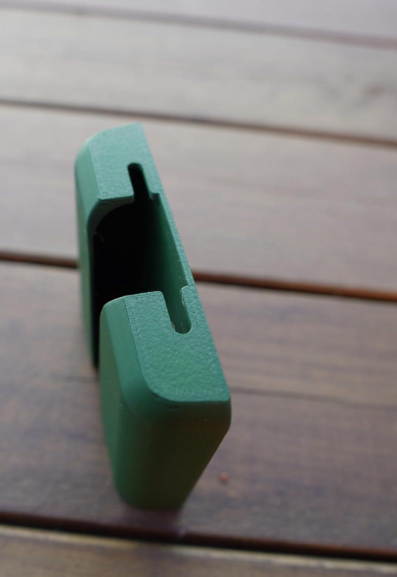 Op de afbeelding: Een matte bosgroene 3D-geprinte kunststof houder met een rechthoekige vorm en een verticale gleuf aan de bovenrand. Het object heeft een getextureerde oppervlakteafwerking en een holle binnenruimte ontworpen voor het vasthouden van een plat item.