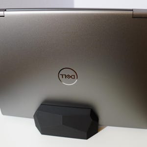 May include: A silver laptop computer with the Dell logo on the back. The laptop is sitting on a black stand.