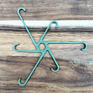 Op de afbeelding: Een zeegroene kledinghanger met een uniek stervormig ontwerp. Het heeft zes armen die uitgaan van een centraal zeshoekig punt. De plastic hanger heeft gebogen haken om kleding op te hangen. Het ontwerp is modern en functioneel.