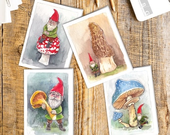 Pode incluir: Conjunto de quatro cartões de felicitação em aquarela com gnomos e cogumelos de fantasia. Cada cartão apresenta uma combinação diferente de gnomo e cogumelo, com um cogumelo vermelho e branco, um cogumelo marrom alto, um cogumelo amarelo e um cogumelo azul.