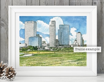 May include: A framed watercolor print of a city skyline, featuring tall buildings under a blue sky with fluffy white clouds. The print is in a white frame and rests on a white surface. The text "frame example" is visible on the print.