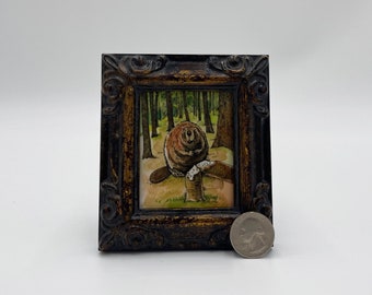 May include: A framed watercolour painting of a beaver sitting on a log in a woodland setting. The beaver is brown and has a white belly. The woodland is green and the log is brown. The painting is in a dark brown frame with gold accents.