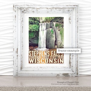 Peut inclure: Une impression encadrée d'une peinture à l'aquarelle de Stephens Falls dans le parc d'État de Governor Dodge, Wisconsin. L'impression représente une cascade qui se précipite sur des rochers avec une végétation luxuriante verte qui l'entoure. Le texte "Stephens Falls", "Governor Dodge State Park" et "Wisconsin" est imprimé dans une police de caractères de style vintage.