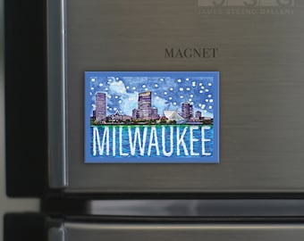 May include: A blue and white magnet featuring a stylized cityscape of Milwaukee, Wisconsin. The city skyline is depicted with white snow falling. The text "MILWAUKEE" is printed in white letters below the cityscape.