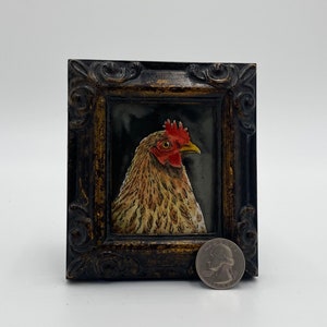 May include: A framed painting of a brown and white chicken with a red comb and wattle. The painting is in a dark wood frame with gold accents.