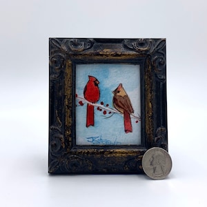 May include: A framed watercolor painting of two cardinals perched on a branch with red berries. The painting is in a black frame with gold accents. The artist's signature, "J. Steen", is visible in the bottom right corner.