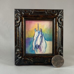 May include: A framed watercolor painting of a white unicorn with a rainbow background. The unicorn has a silver horn and a long flowing mane. The painting is in a dark brown frame with ornate details.