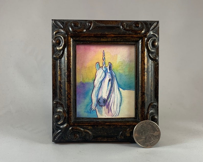 May include: A framed watercolor painting of a white unicorn with a rainbow background. The unicorn has a silver horn and a long flowing mane. The painting is in a dark brown frame with ornate details.
