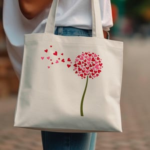 May include: A white canvas tote bag with a pink and red heart dandelion design. The dandelion is blowing away with hearts floating in the air.