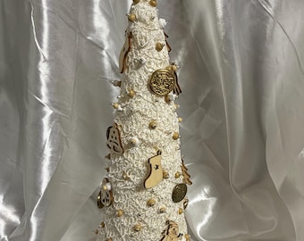 May include: A handmade, off-white Christmas tree with a crocheted texture. It is adorned with wooden ornaments, gold beads, and a star topper. The tree is approximately 10 inches tall, perfect for holiday decor.