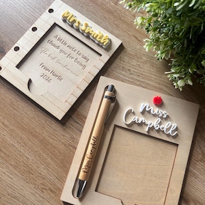 Puede incluir: Dos soportes rectangulares de madera para notas con recortes. Uno presenta el nombre Mrs Smith en amarillo, con el texto grabado A little note to say thank you for being The best teacher ever From Harlie 2026. El otro tiene Miss Campbell en blanco, un icono de manzana roja y un bolígrafo de bambú grabado con Miss Campbell.