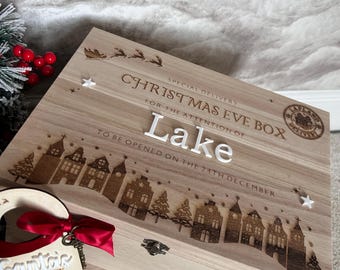 May include: A light-colored wooden Christmas Eve box with engraved text and a village scene. The lid features the name Lake, a Lapland delivery stamp, and a sleigh. A wooden tag with a red ribbon and a metal key reads Santa's Magic Key.
