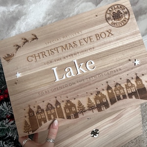 May include: A rectangular wooden Christmas Eve box featuring laser-engraved text that reads Special Delivery, Christmas Eve Box, For the attention of Lake, and To be opened on the 24th December. It includes a Lapland Delivery stamp and a village scene.