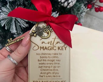 May include: A wooden Christmas ornament with the text "Santa's Magic Key" and a poem. The ornament is attached to a decorative antique-style key with a red satin bow. The background includes a Christmas tree with red berries and pinecones.