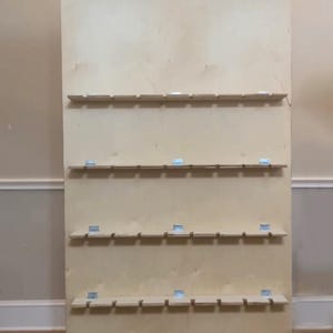 Puede incluir: Un gran tablero de exhibici&oacute;n de madera sin terminar con m&uacute;ltiples filas de peque&ntilde;os estantes. Cada estante est&aacute; soportado por soportes met&aacute;licos. La madera tiene un color claro y natural, y el dise&ntilde;o sugiere que es para organizar o exhibir art&iacute;culos.
