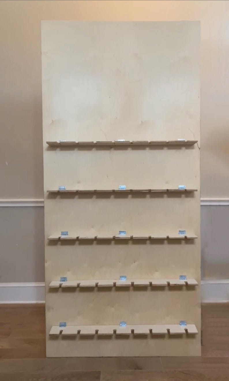 Puede incluir: Un gran tablero de exhibici&oacute;n de madera sin terminar con m&uacute;ltiples filas de peque&ntilde;os estantes. Cada estante est&aacute; soportado por soportes met&aacute;licos. La madera tiene un color claro y natural, y el dise&ntilde;o sugiere que es para organizar o exhibir art&iacute;culos.