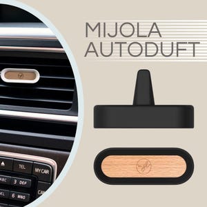 May include: An air freshener with a wooden insert and the text "MIJOLA AUTODUFT". The air freshener is shown in a car's air vent and also displayed separately. The wooden insert has a logo. The air freshener is black and white.