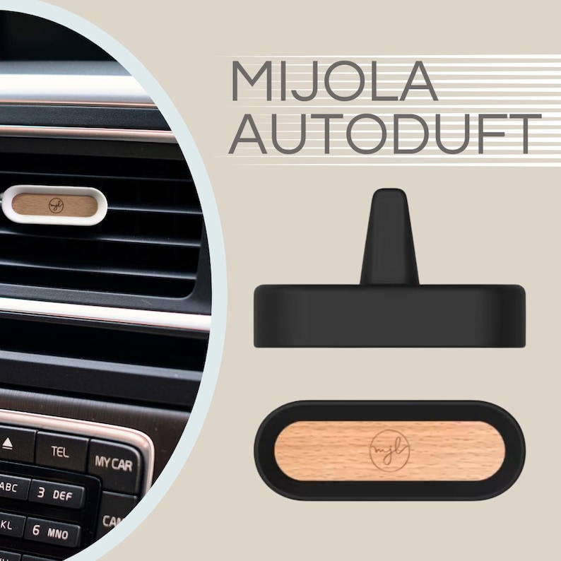 May include: An air freshener with a wooden insert and the text "MIJOLA AUTODUFT". The air freshener is shown in a car's air vent and also displayed separately. The wooden insert has a logo. The air freshener is black and white.