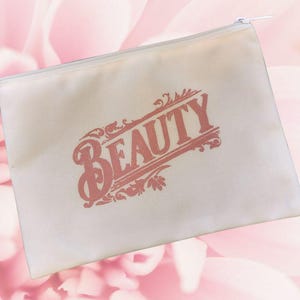 May include: A cream-colored canvas cosmetic bag with a zipper closure. The word "BEAUTY" is printed in a decorative, coral-colored font across the front of the bag. The background is a soft pink floral pattern.