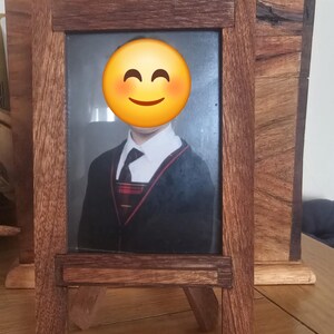 Puede incluir: Un marco de fotos de madera marrón oscuro con un retrato. El marco tiene forma rectangular y es de madera. El retrato muestra a una persona con blazer y corbata. El marco está sobre una superficie de madera.