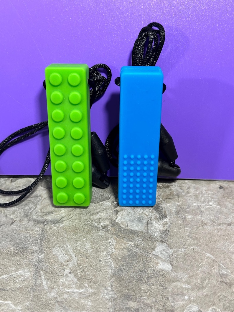 adult chewelry chew necklace - looks like a building brick block on the front and soothing bumps on the back. has a safety break away necklace. colors are: blue or green