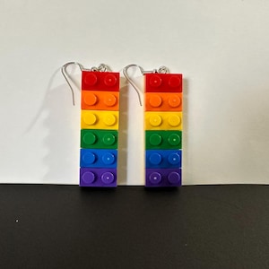 May include: Rainbow colored Lego brick earrings. Each earring is made of seven stacked Lego bricks in the colors red, orange, yellow, green, blue, indigo, and violet.
