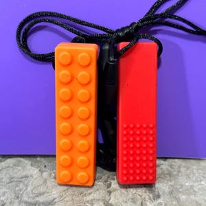 adult chewelry chew necklace - looks like a building brick block on the front and soothing bumps on the back. has a safety break away necklace. colors are: orange or yellow