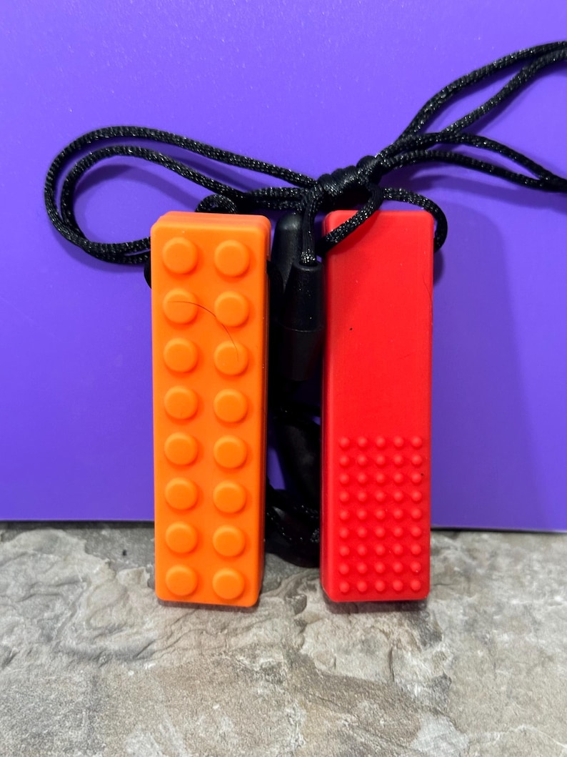 adult chewelry chew necklace - looks like a building brick block on the front and soothing bumps on the back. has a safety break away necklace. colors are: orange or yellow