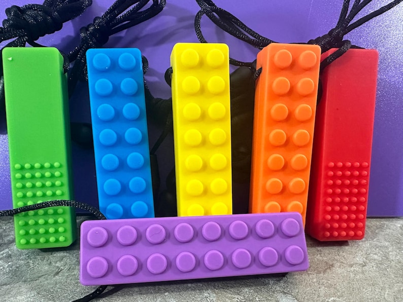 adult chewelry chew necklace - looks like a building brick block on the front and soothing bumps on the back. has a safety break away necklace. colors are: Red, orange. yellow, blue. green, purple