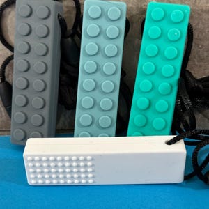 adult chewelry chew necklace - looks like a building brick block on the front and soothing bumps on the back. has a safety break away necklace. colors are: tan, light blue, turquoise, or white