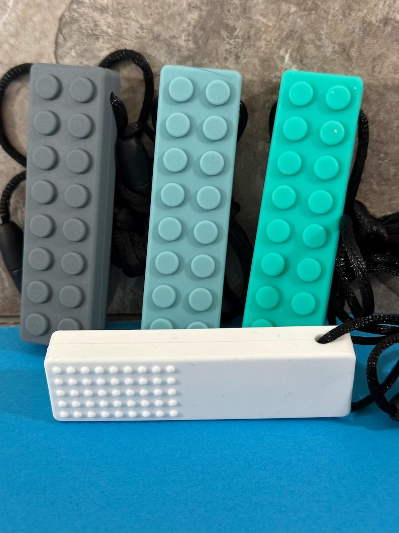 adult chewelry chew necklace - looks like a building brick block on the front and soothing bumps on the back. has a safety break away necklace. colors are: tan, light blue, turquoise, or white