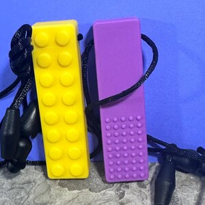 adult chewelry chew necklace - looks like a building brick block on the front and soothing bumps on the back. has a safety break away necklace. colors are: yellow or purple