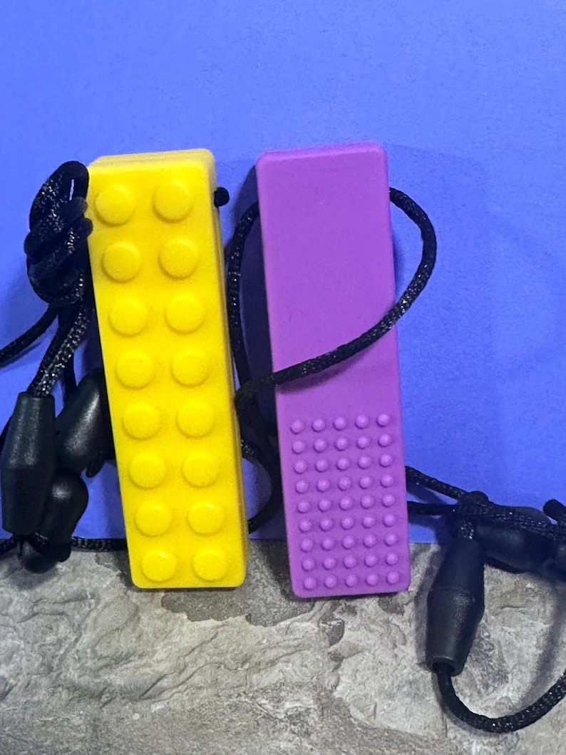 adult chewelry chew necklace - looks like a building brick block on the front and soothing bumps on the back. has a safety break away necklace. colors are: yellow or purple