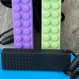 adult chewelry chew necklace - looks like a building brick block on the front and soothing bumps on the back. has a safety break away necklace. colors are: lavender, light green or black