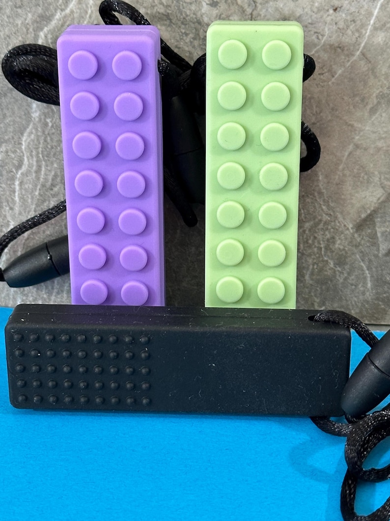 adult chewelry chew necklace - looks like a building brick block on the front and soothing bumps on the back. has a safety break away necklace. colors are: lavender, light green or black