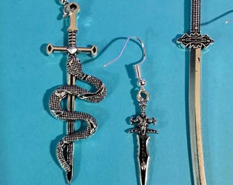 May include: Three pairs of silver-colored earrings with different sword designs. One earring features a snake wrapped around a sword, another a dagger, and the third a long sword. The earrings are displayed on a blue background.