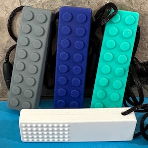 adult chewelry chew necklace - looks like a building brick block on the front and soothing bumps on the back. has a safety break away necklace. colors are: gray, dark blue. turquoise, or white