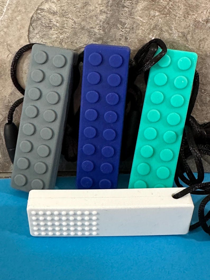 adult chewelry chew necklace - looks like a building brick block on the front and soothing bumps on the back. has a safety break away necklace. colors are: gray, dark blue. turquoise, or white