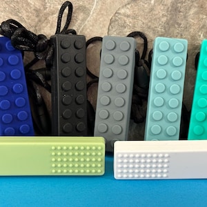 adult chewelry chew necklace - looks like a building brick block on the front and soothing bumps on the back. has a safety break away necklace. colors are: dark navy blue, black, gray, light blue, turquoise, light green, white