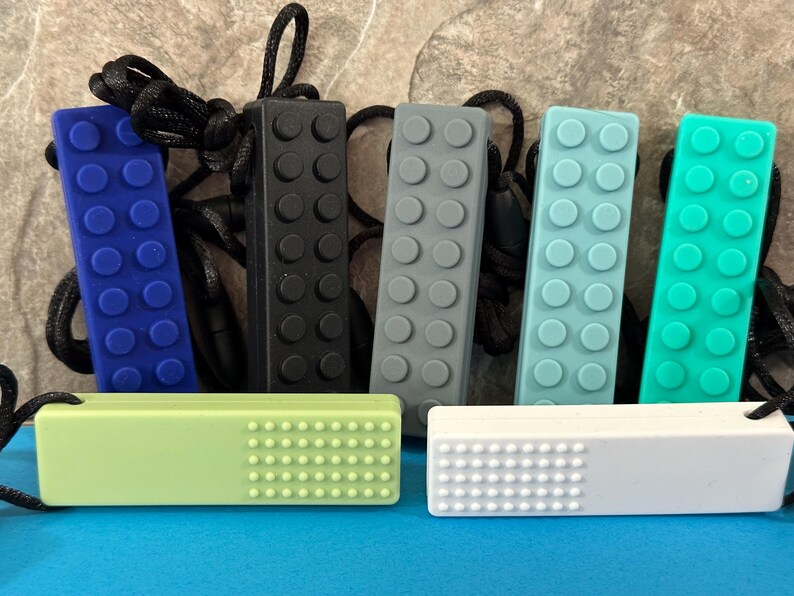 adult chewelry chew necklace - looks like a building brick block on the front and soothing bumps on the back. has a safety break away necklace. colors are: dark navy blue, black, gray, light blue, turquoise, light green, white